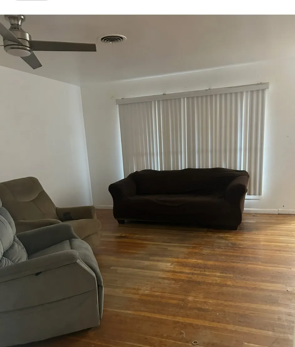 Hardwood flooring throughout, with a ceiling fan and vertical window blinds