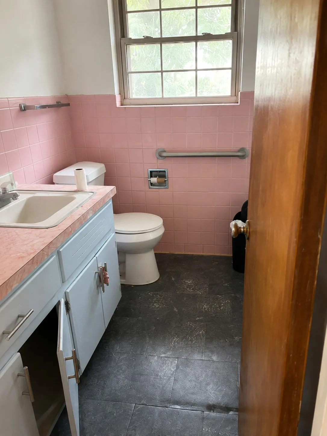 Bathroom featuring pink subway tile walls, pedestal sink with wood-finish cabinetry, toilet, and dark tile flooring