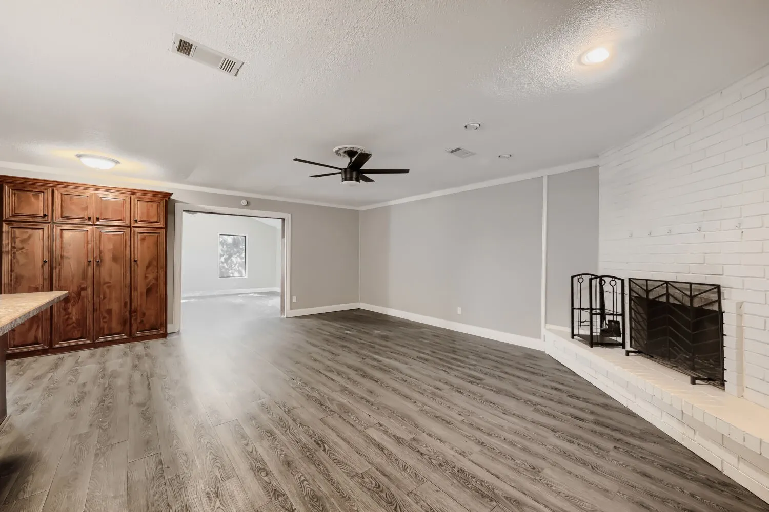 Wood-finish flooring, white brick fireplace, built-in cabinetry, ceiling fan, and recessed lighting