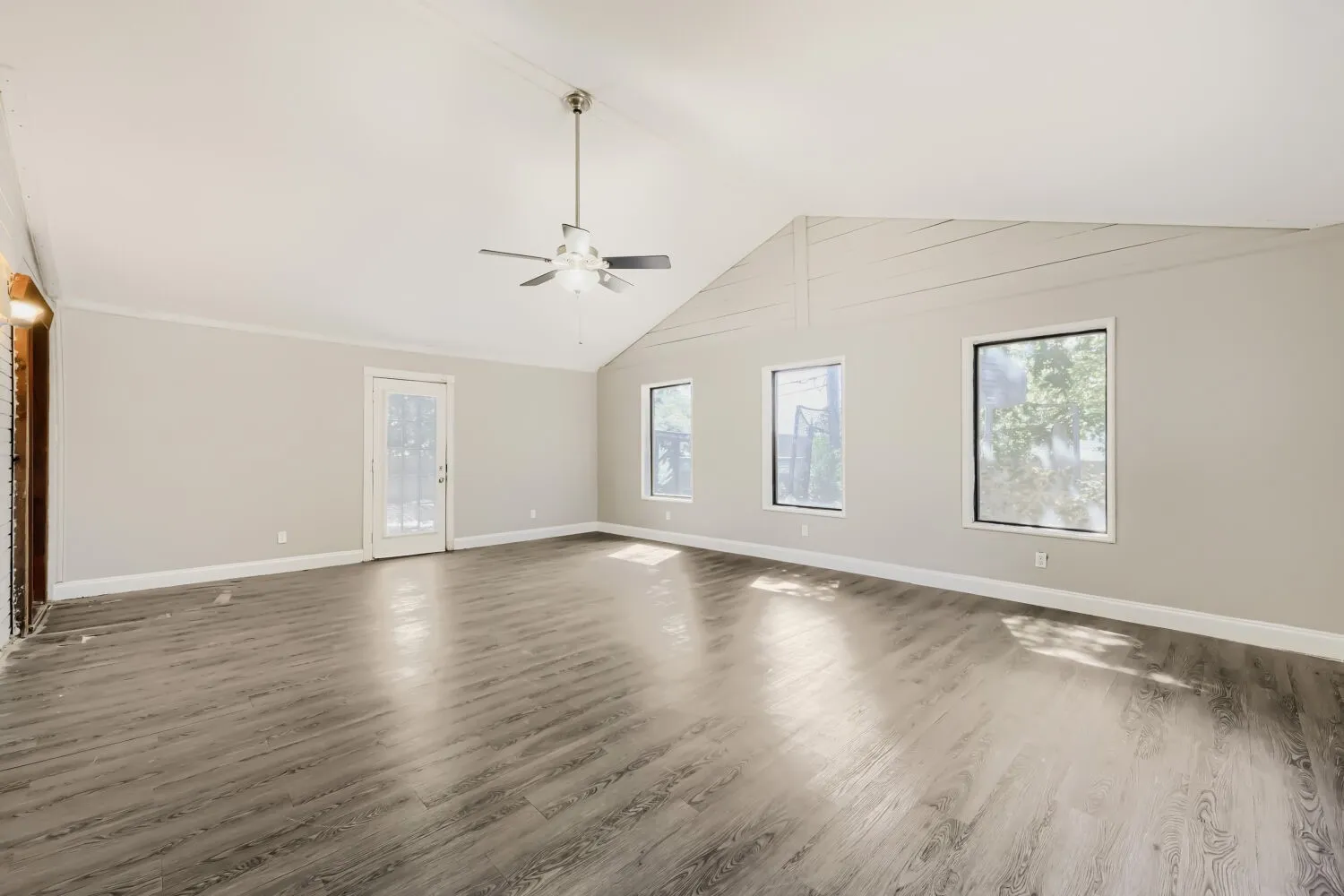Vaulted ceiling with a ceiling fan, wood-finish flooring, multiple windows, and a glass-paneled door