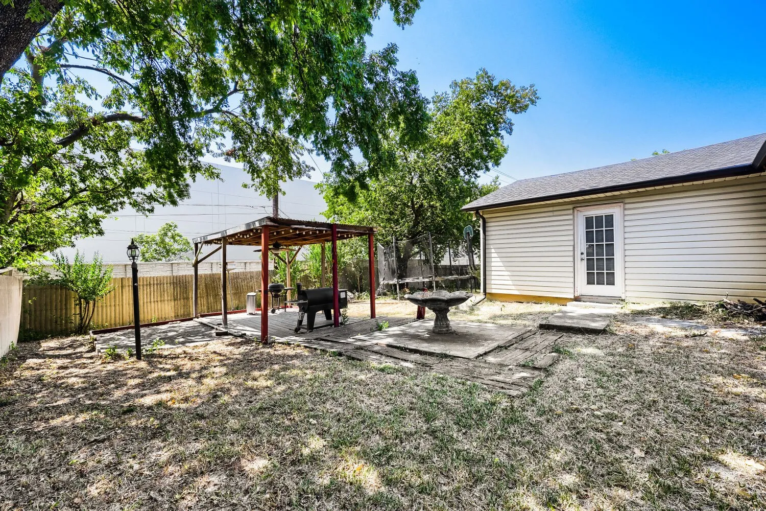Spacious backyard retreat featuring mature shade trees, a rustic pergola structure with seating area, and expansive gravel landscape