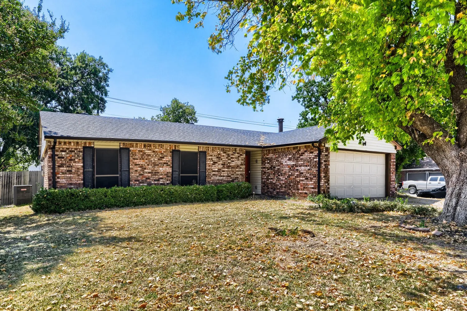 Brick exterior featuring a gabled roofline, attached garage, and mature landscaping
