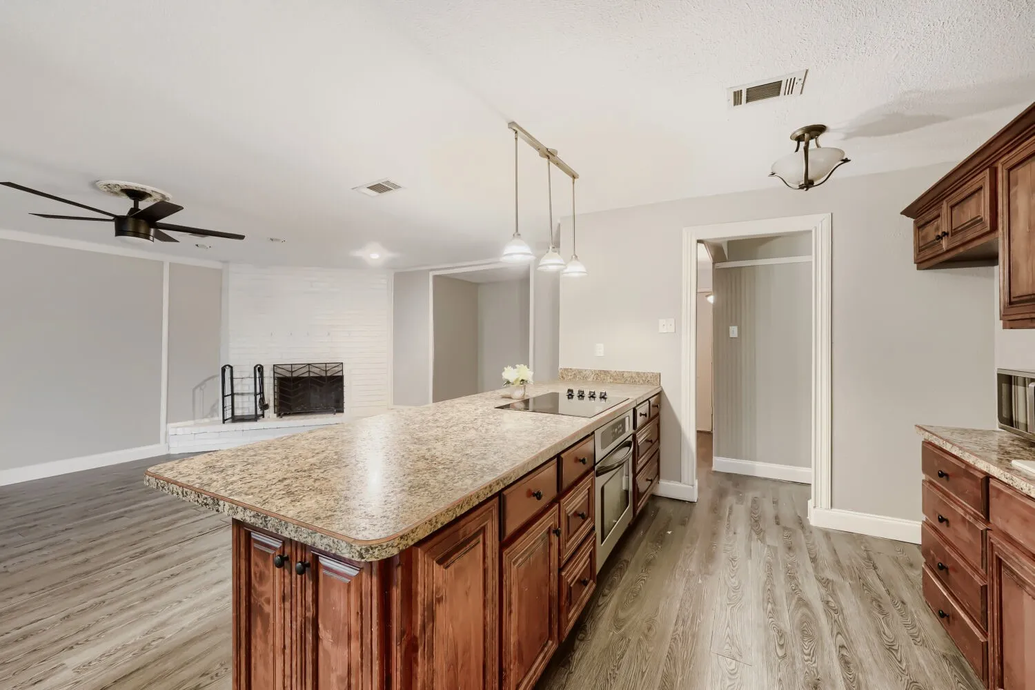 Kitchen island with integrated cooktop, wood-finish flooring, white brick fireplace, ceiling fan, and pendant lighting