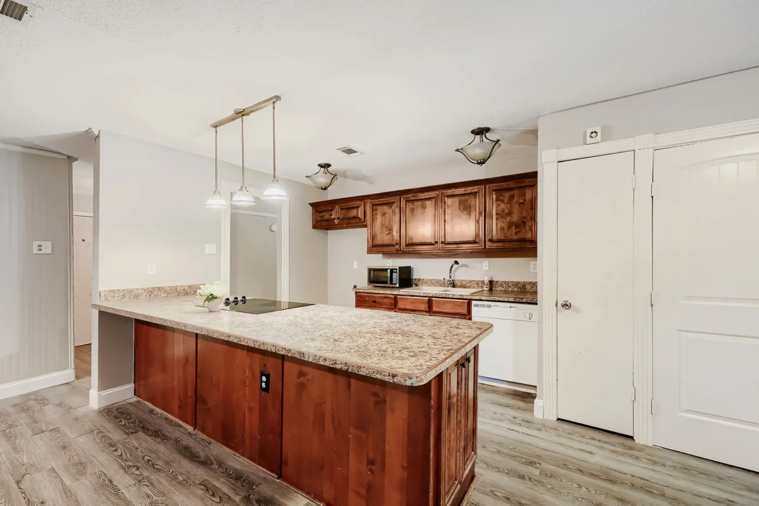 Kitchen featuring a center island with a built-in cooktop, light-toned countertops, wood-finish cabinetry, and wood-finish flooring