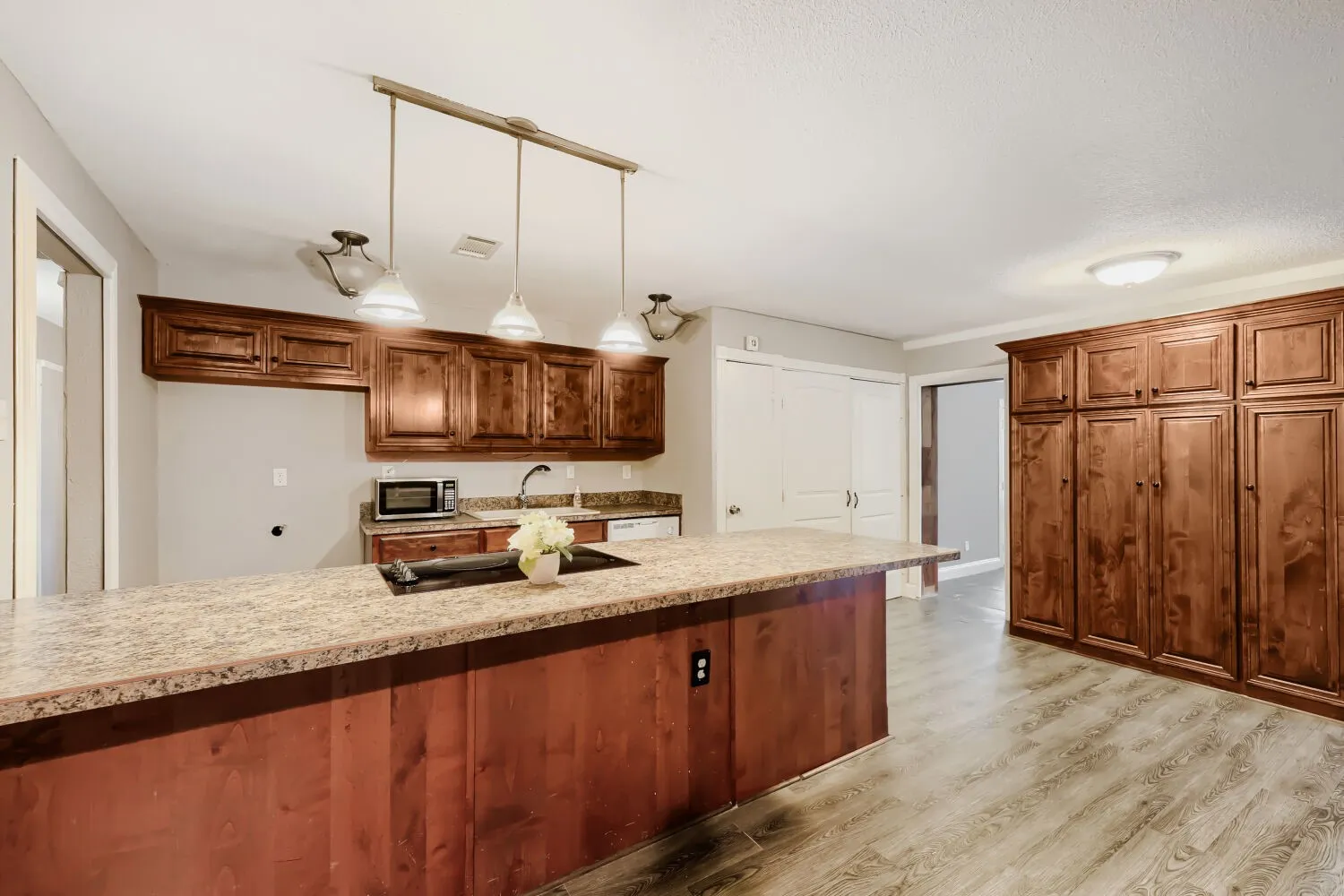 Kitchen with a large island featuring a cooktop, wood-finish flooring, and extensive wood cabinetry