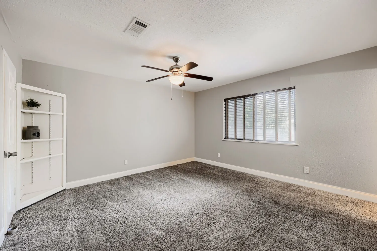 Plush carpeting, window with blinds, ceiling fan, and built-in shelving