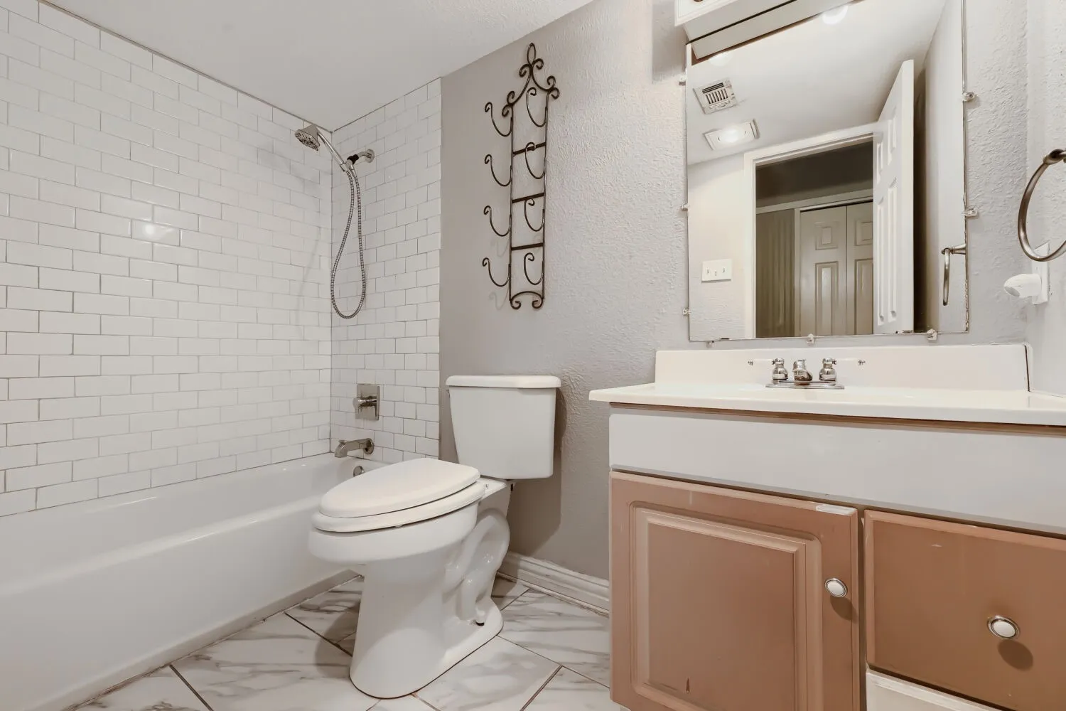 White subway tile shower surround, chrome shower fixtures, built-in bathtub, vanity with integrated sink, and a framed mirror