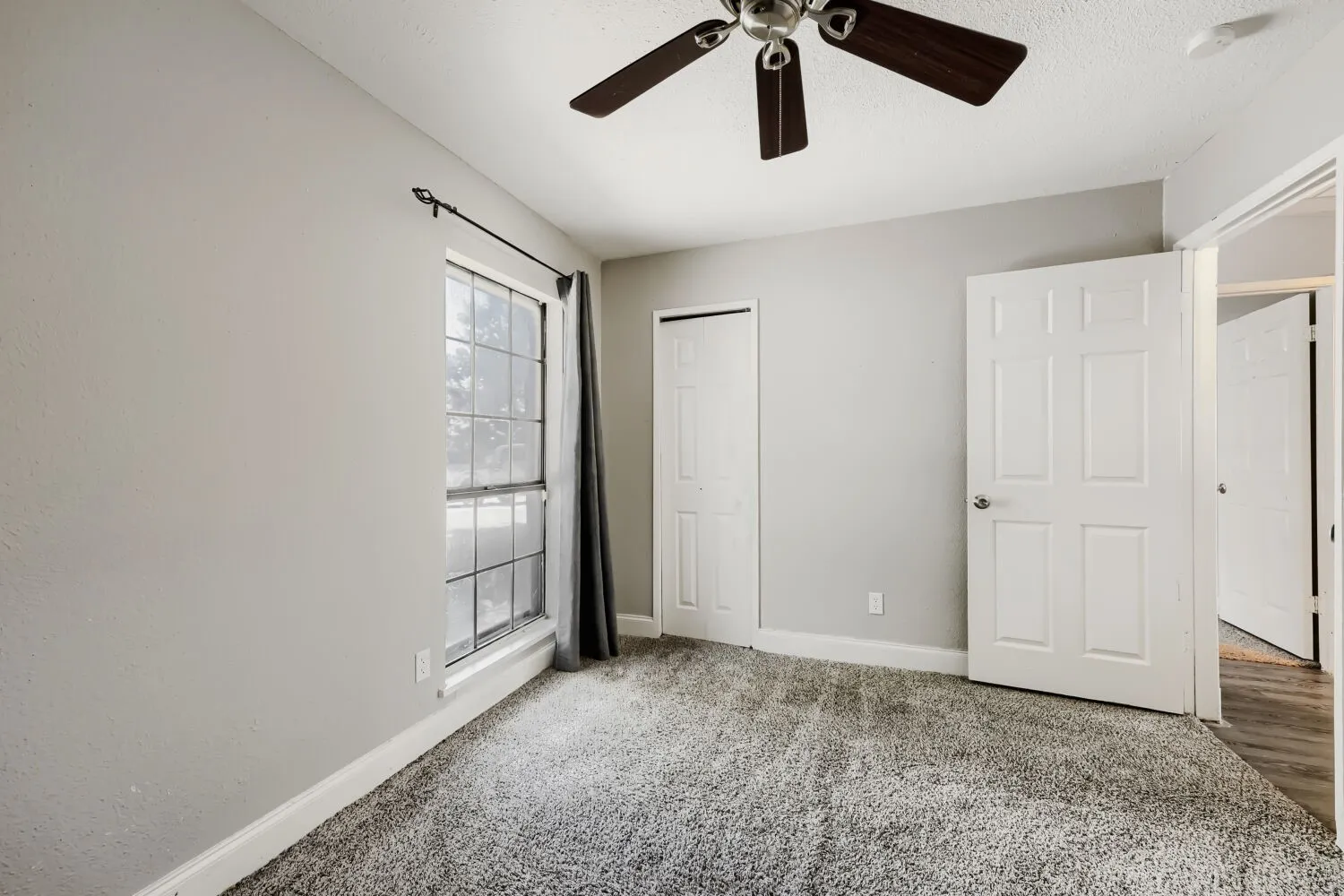 Bright bedroom featuring neutral wall finishes, carpeted flooring, a ceiling fan with integrated lighting, large double-door closet with six-panel doors, and a window with natural light and custom window treatments
