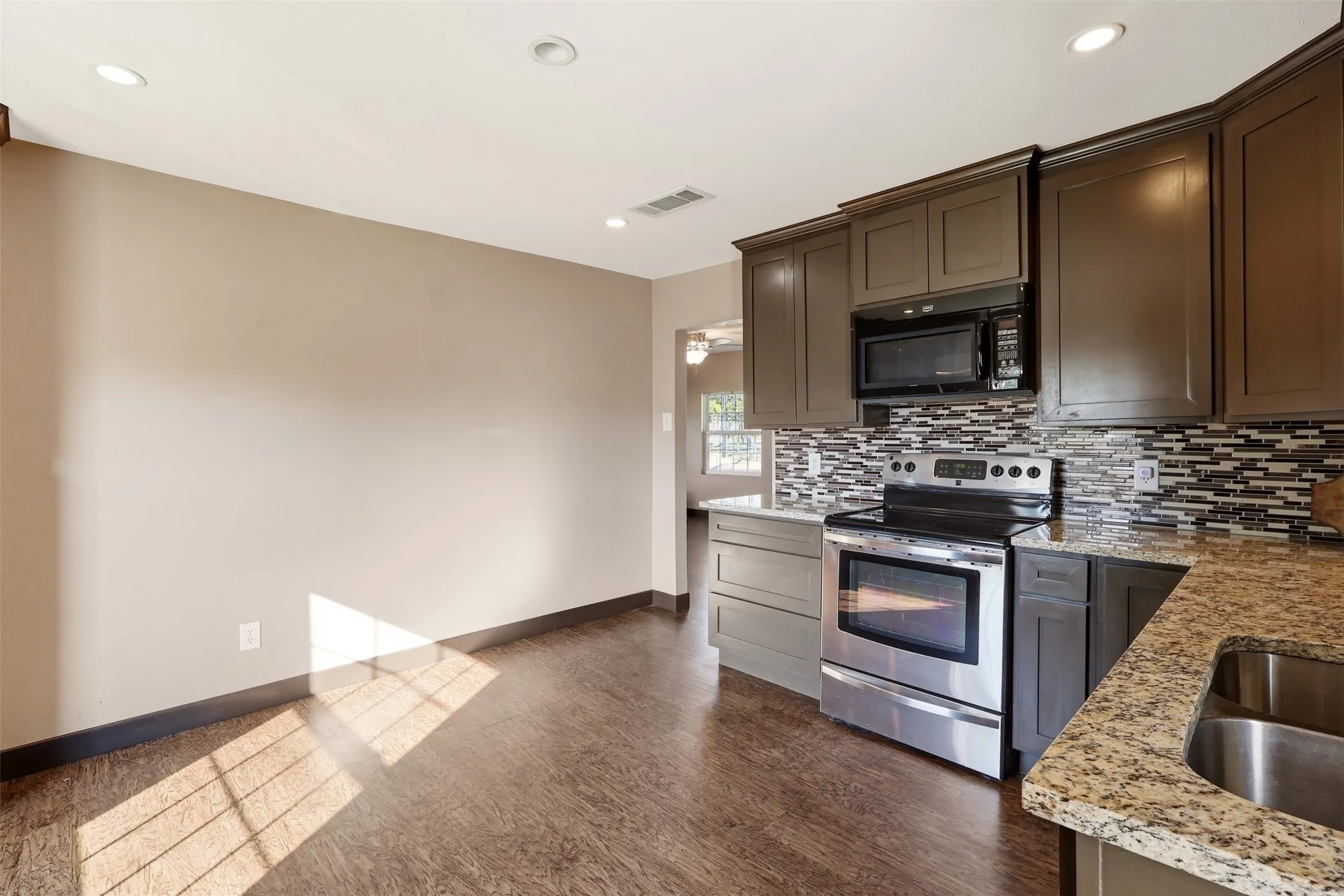Kitchen featuring stainless steel appliances, dark wood-finish cabinetry, granite countertops, and mosaic tile backsplash