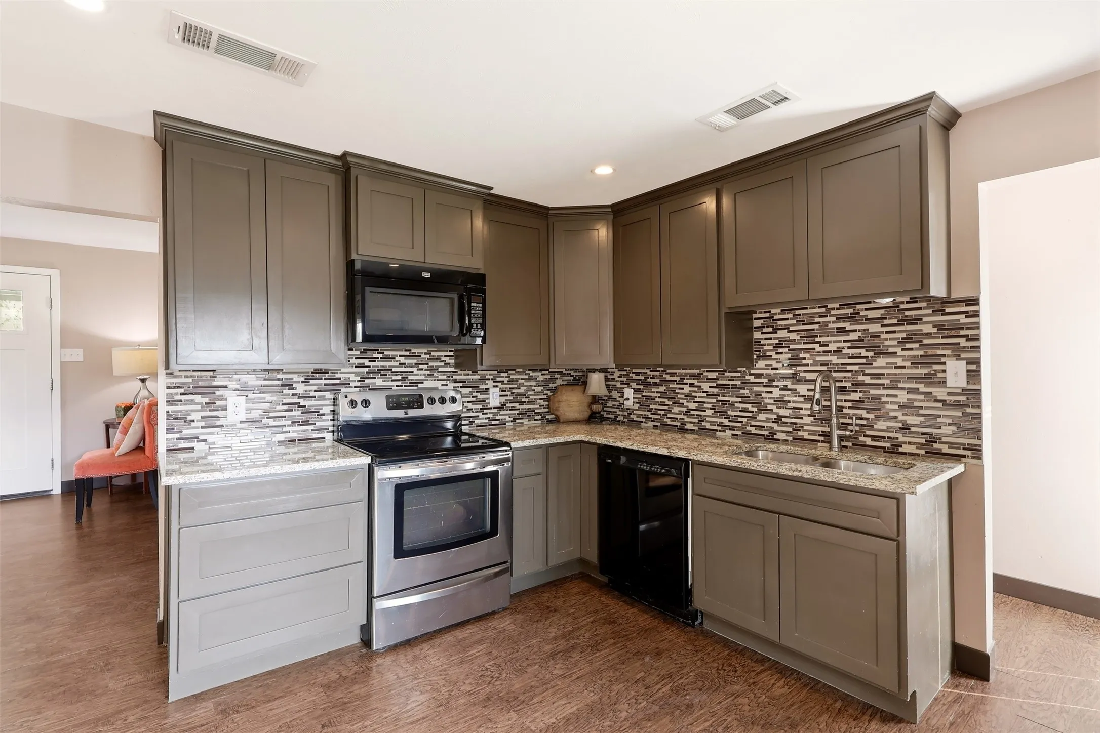 Kitchen featuring wood-finish flooring, L-shaped cabinetry with upper and lower storage, mosaic tile backsplash, stainless steel appliances, and a double basin sink