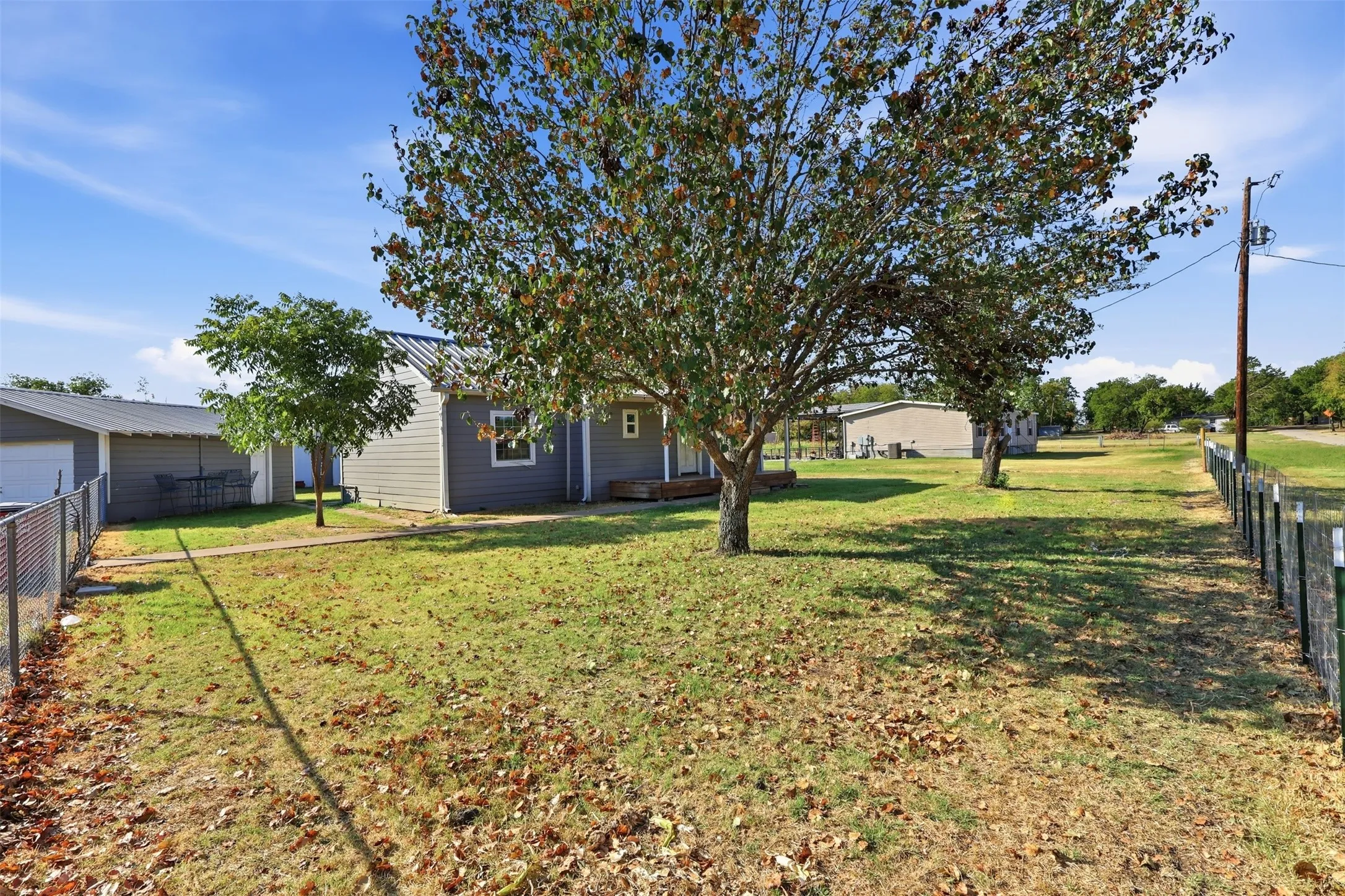 Expansive lawn with mature trees, chain-link fencing, and a detached structure with a metal roof