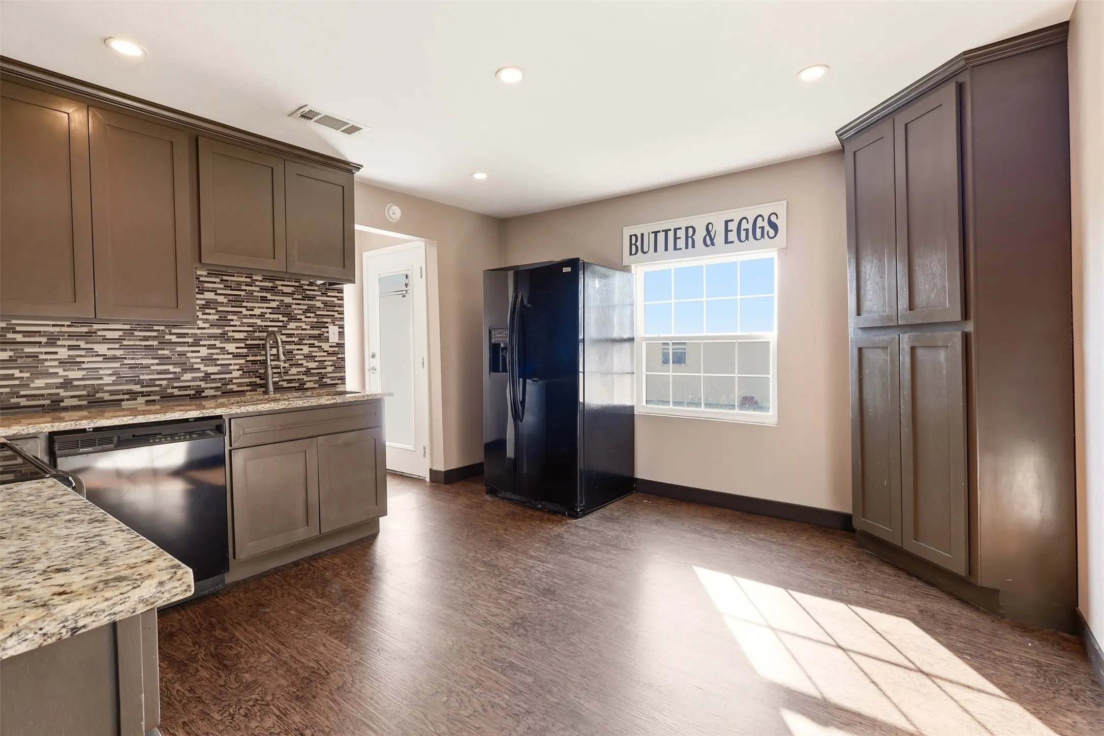 Kitchen featuring wood-finish flooring, granite countertops, and a mosaic tile backsplash