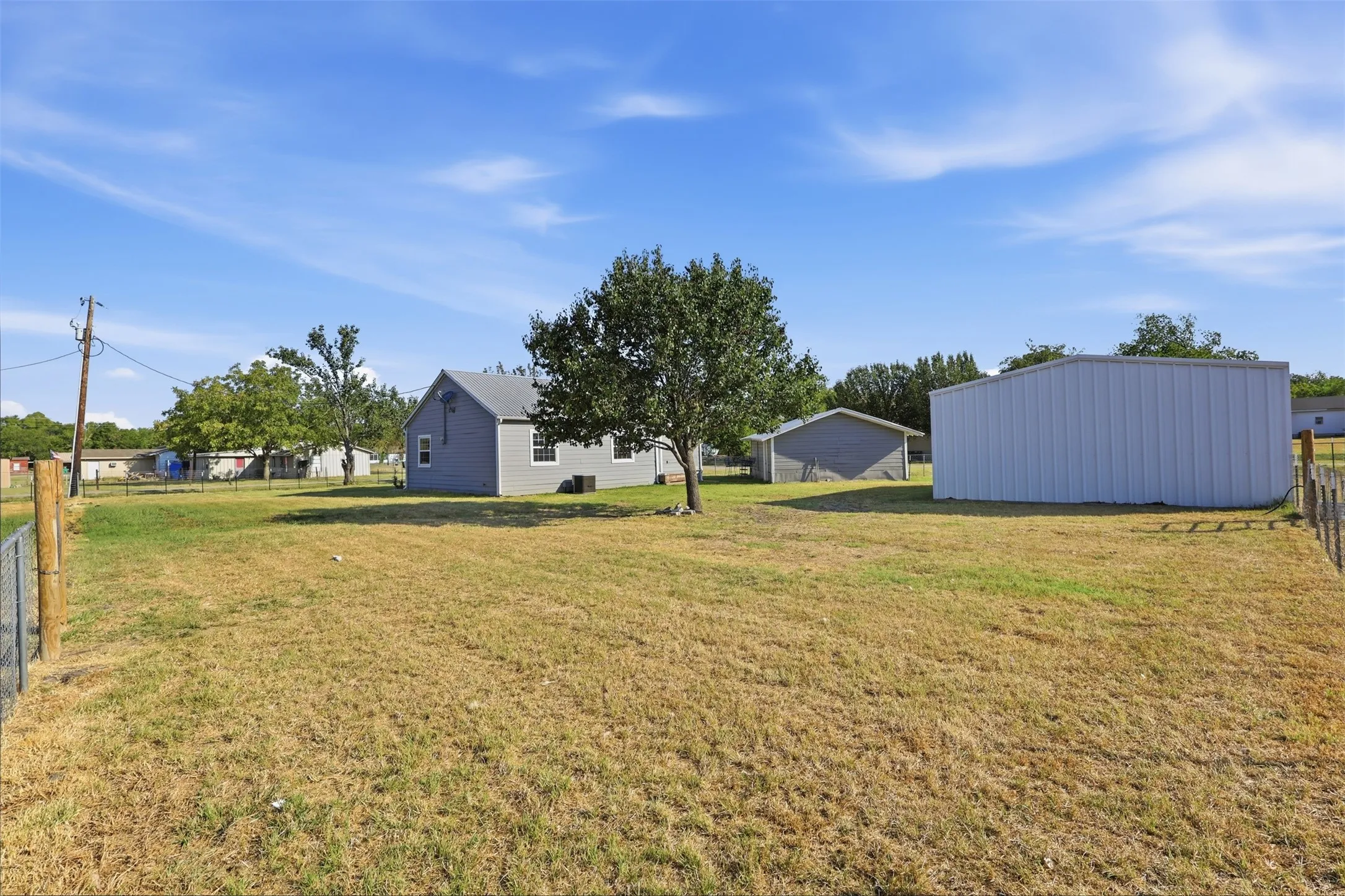 Expansive grassy yard area with a chain-link fence and a large metal outbuilding