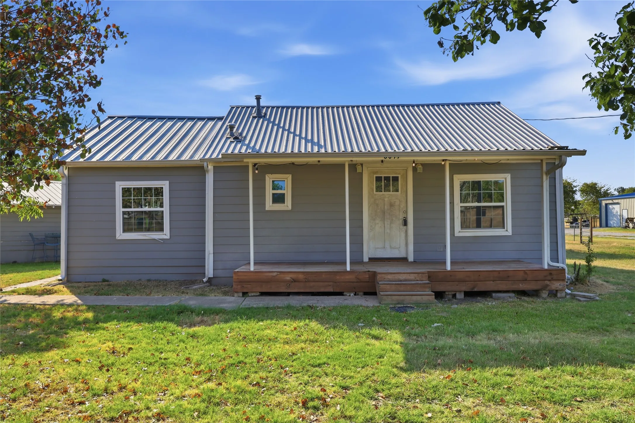 Charming cottage-style home featuring a standing-seam metal roof, horizontal siding exterior, and a covered front porch with columns