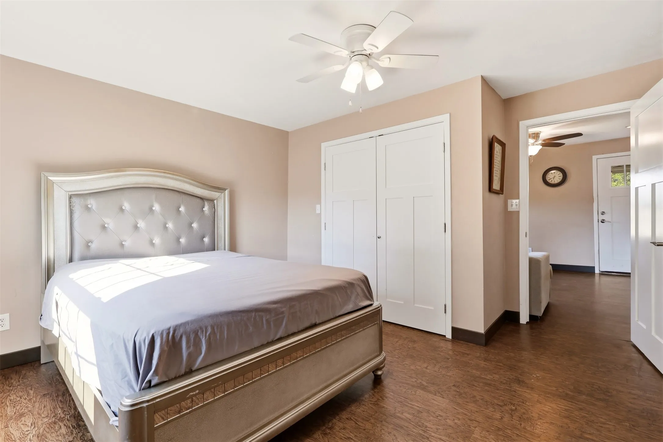 Wood-finish flooring, neutral wall tones, white ceiling fan, and white paneled bi-fold closet doors