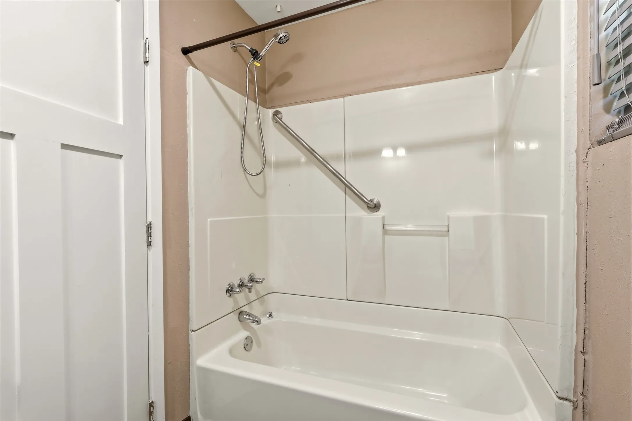 White tub and shower combination with a curved shower rod and grab bar