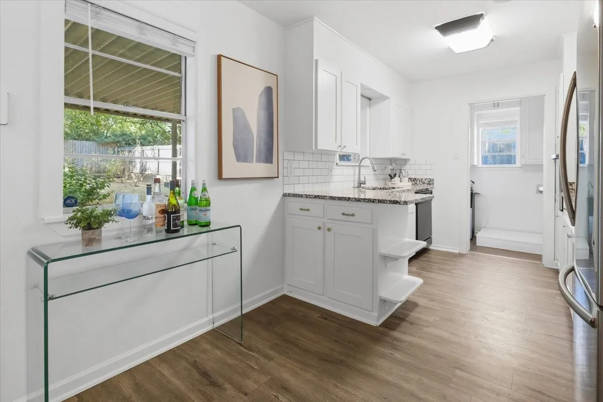 Kitchen featuring white cabinetry, subway tile backsplash, granite countertops, and vinyl wood-finish flooring
