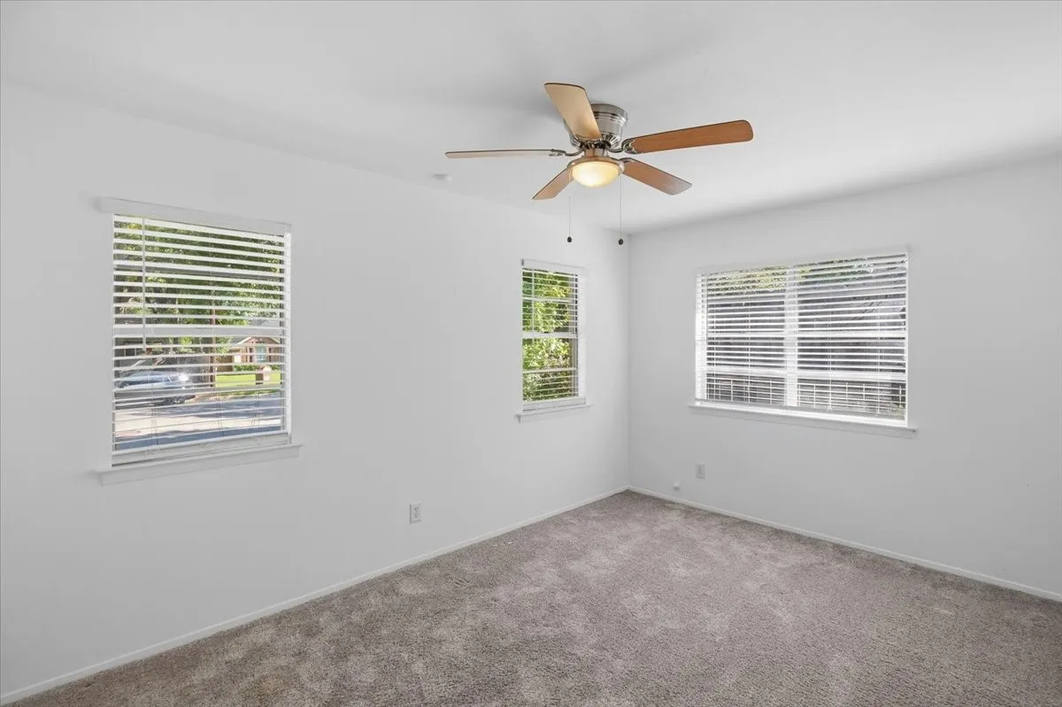 Carpeted flooring, white walls, two windows with blinds, and a ceiling fan with light fixture