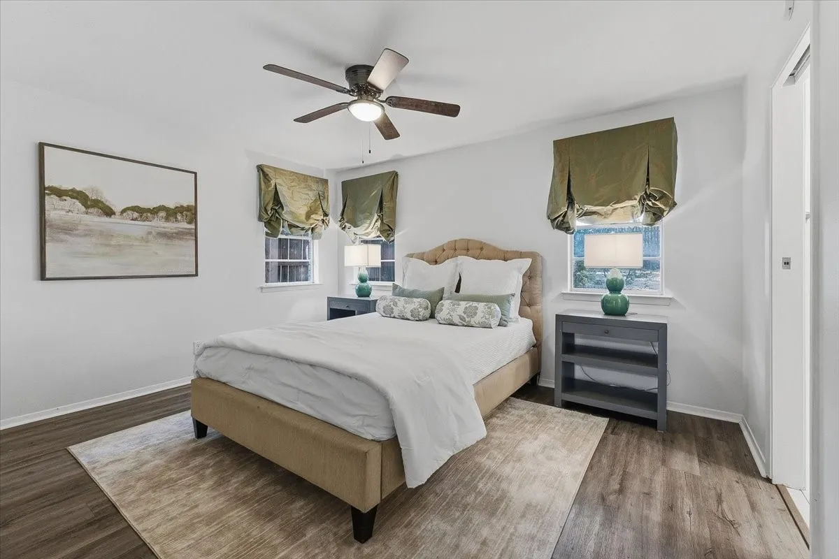 Wood-finish flooring, ceiling fan with light fixture, and windows with window treatments