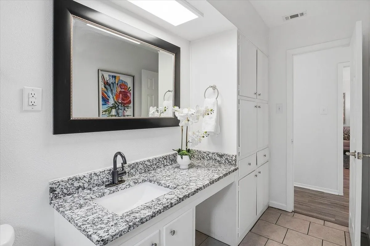 Spa-inspired bathroom featuring a granite speckled countertop with an undermount sink, matte black faucet, and ample storage cabinetry