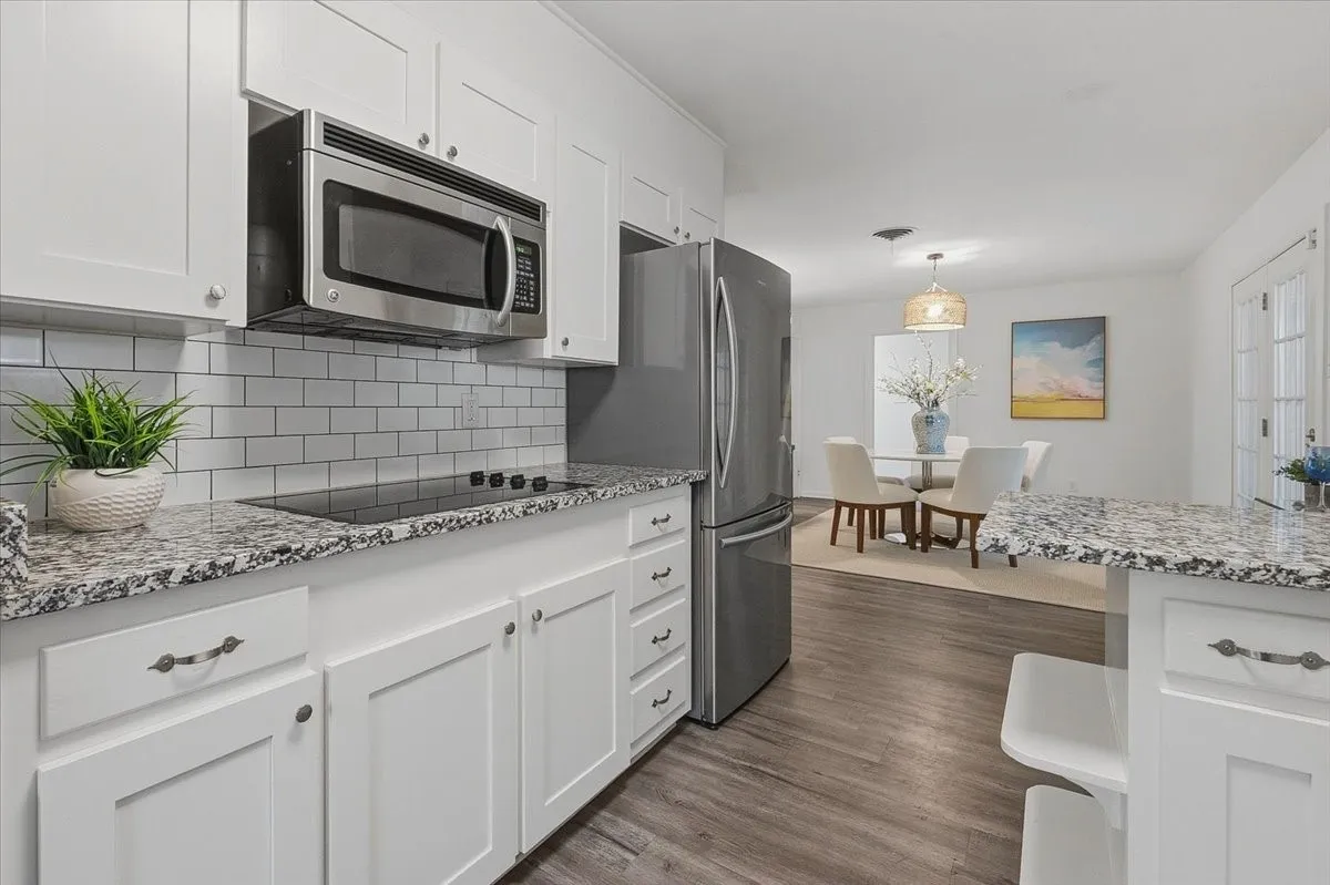 White shaker cabinetry, stainless steel appliances, granite countertops, subway tile backsplash, and vinyl wood-finish flooring