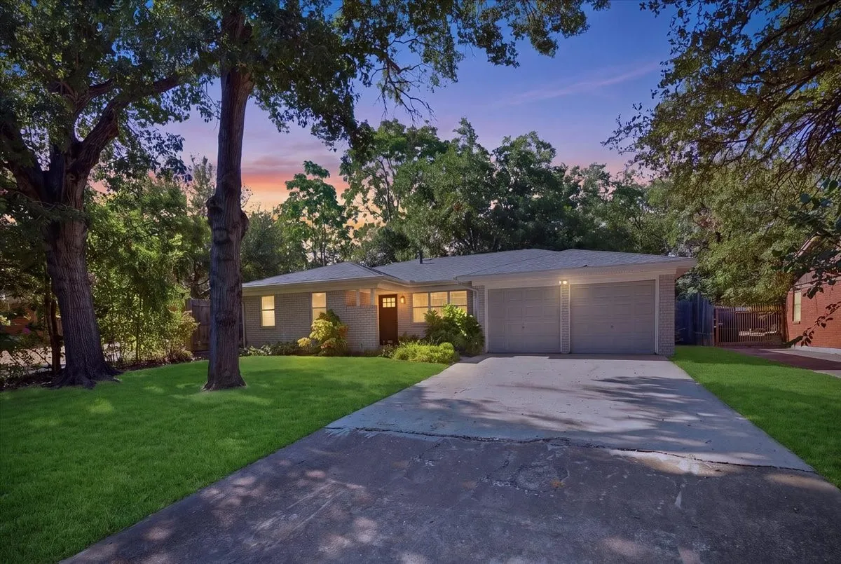 Light-colored brick exterior with an attached two-car garage, concrete driveway, and established front yard landscaping