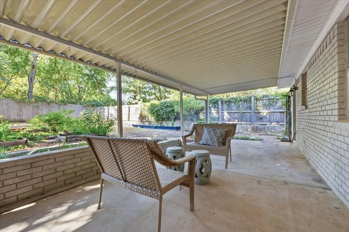 Expansive covered patio with concrete flooring, brick planter, and a fully fenced yard