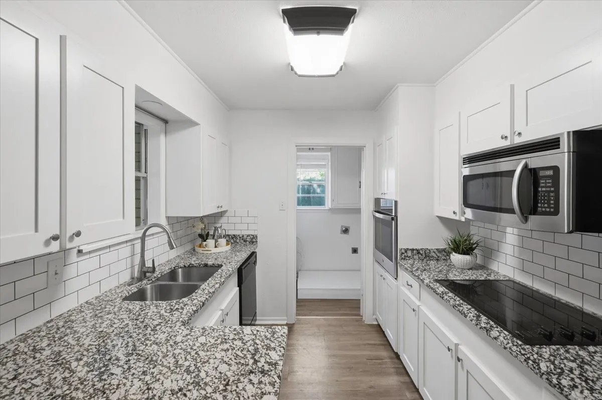 White shaker cabinetry, speckled countertops, stainless steel appliances, subway tile backsplash, and vinyl wood-finish flooring