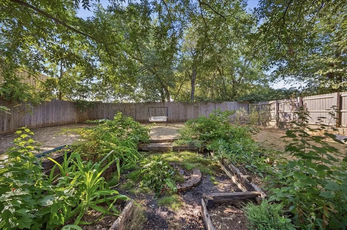 Expansive backyard with a full privacy fence, mature trees providing canopy, and terraced garden beds