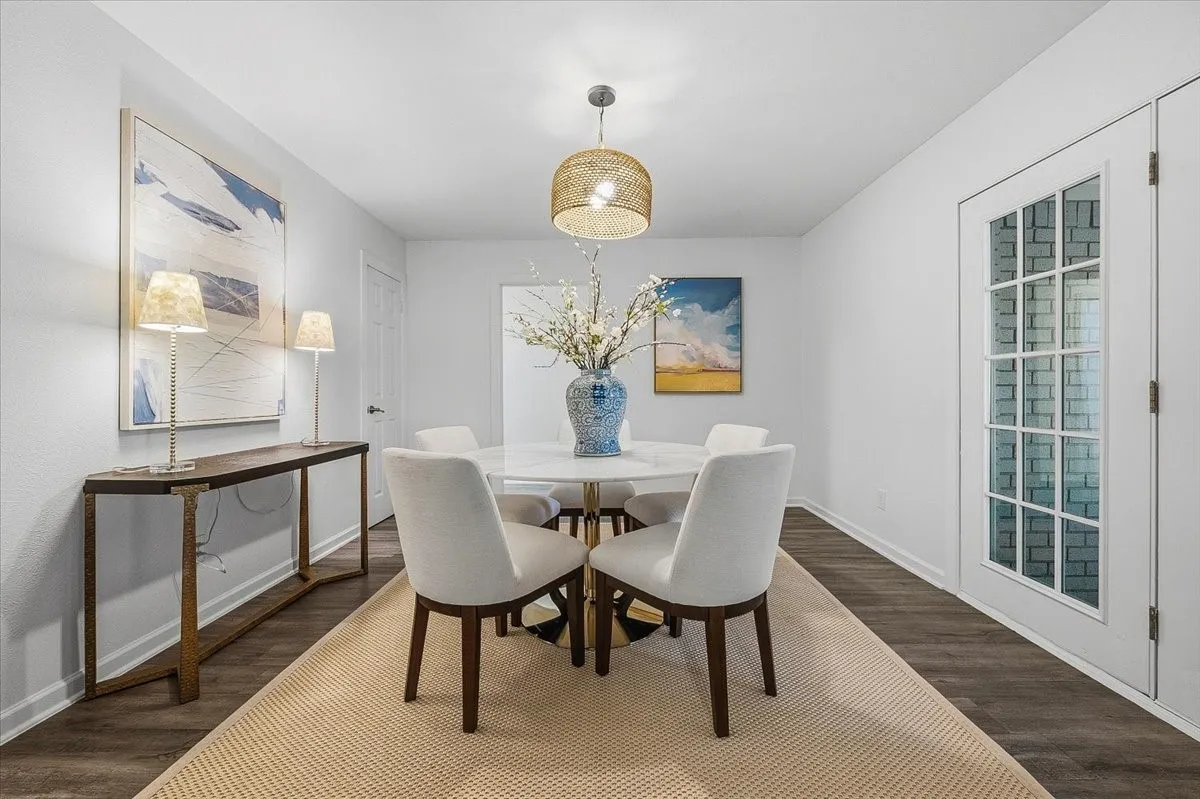 Elegant dining room showcasing a round wood-base table, cream upholstered chairs, and dark wood-finish flooring anchored by a neutral area rug