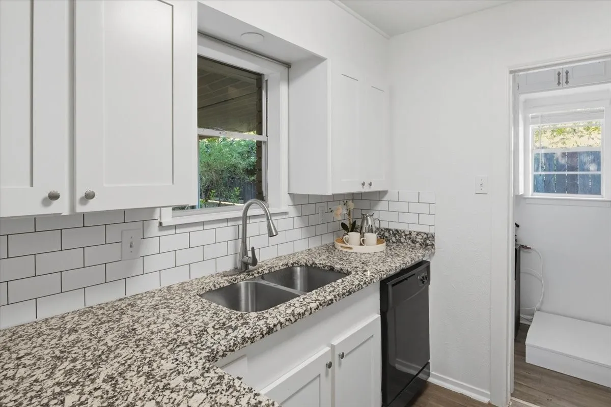 White shaker-style cabinetry, subway tile backsplash, granite-style countertops, stainless steel double-basin sink with gooseneck faucet, and integrated dishwasher