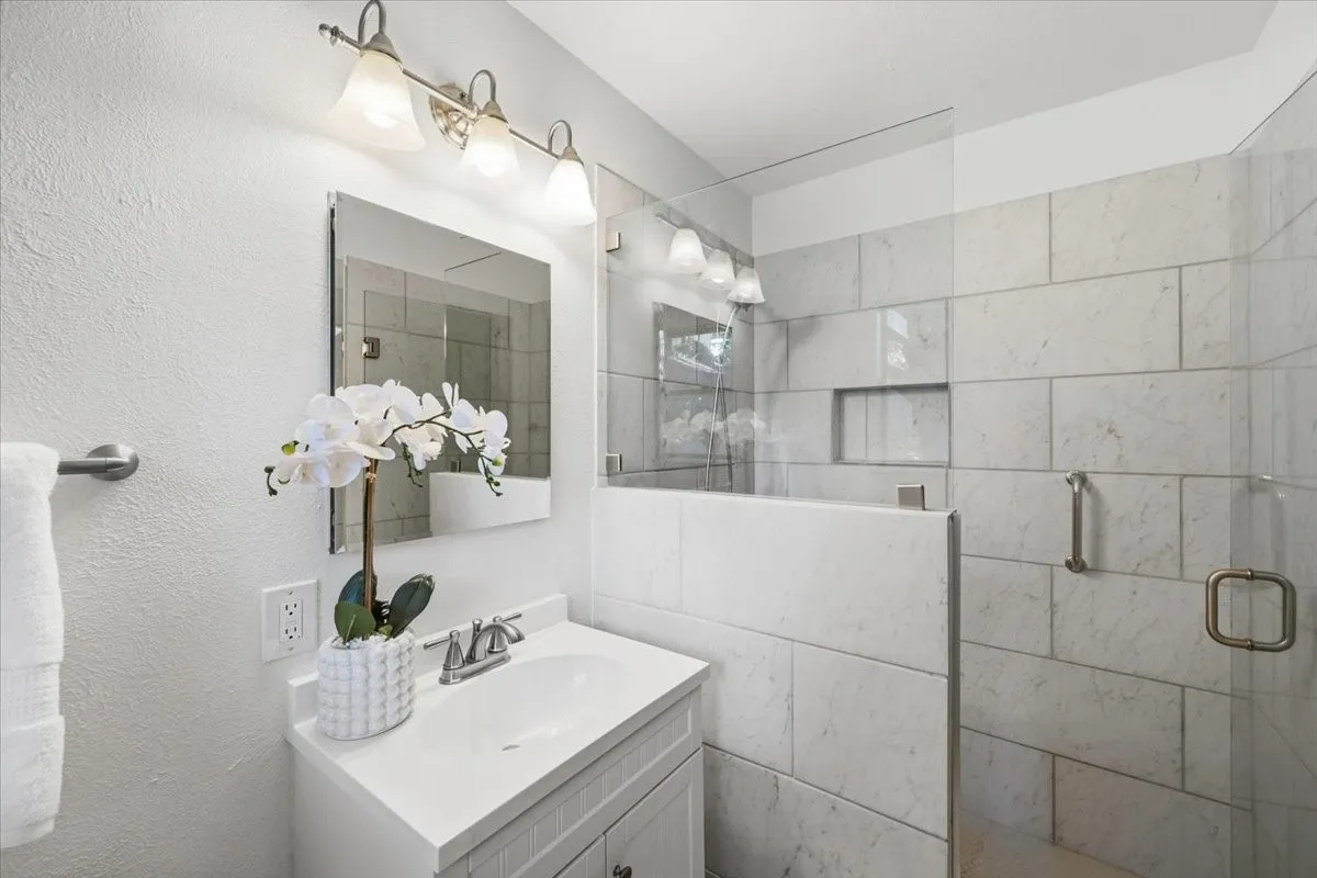 Modern bathroom featuring a single vanity, a frameless glass shower enclosure, a recessed shower niche, and large format wall tile