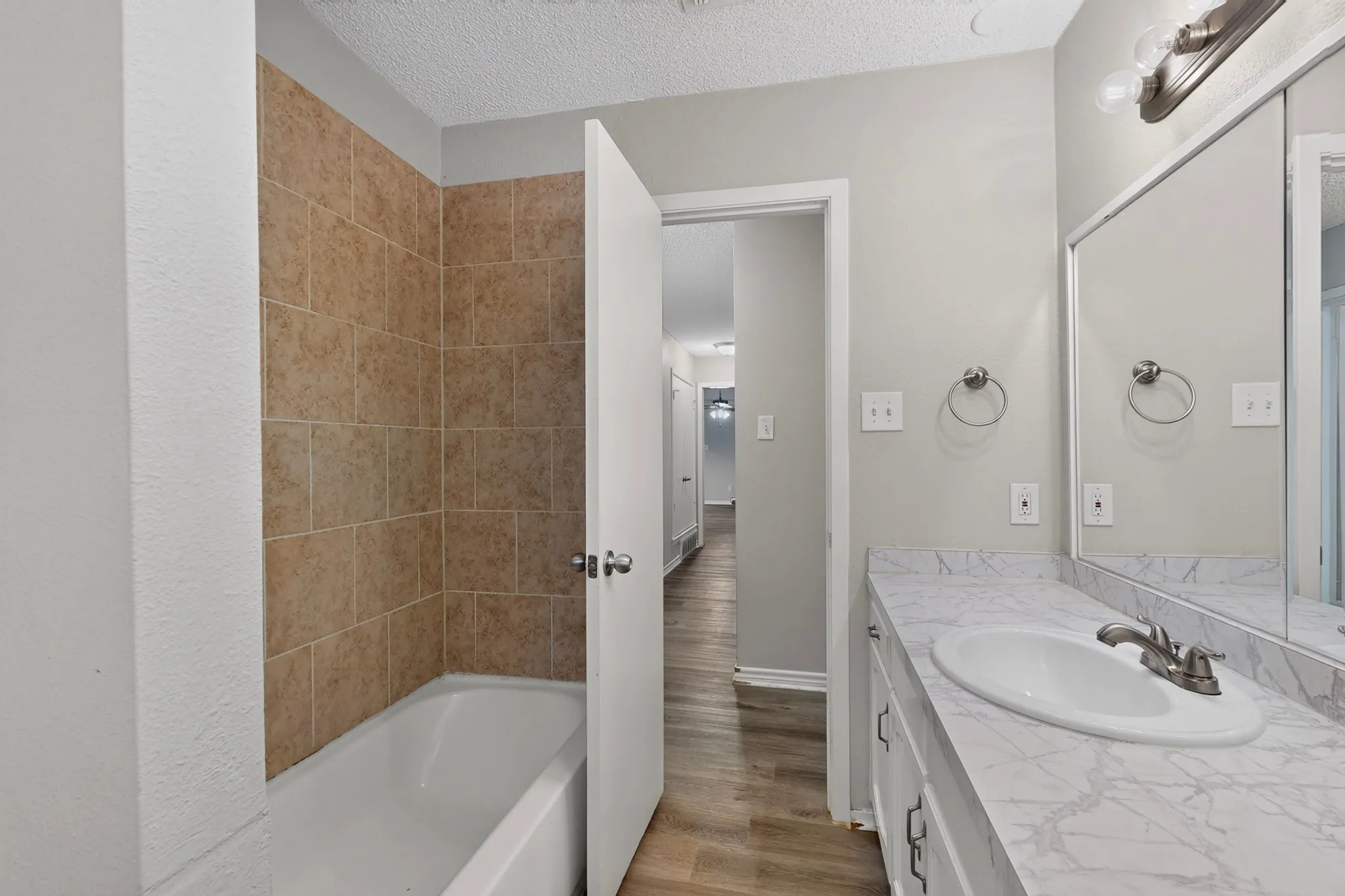 Bathroom featuring a built-in bathtub with brown tiled surround, single vanity with integrated sink, chrome-finish faucet, and an illuminated medicine cabinet