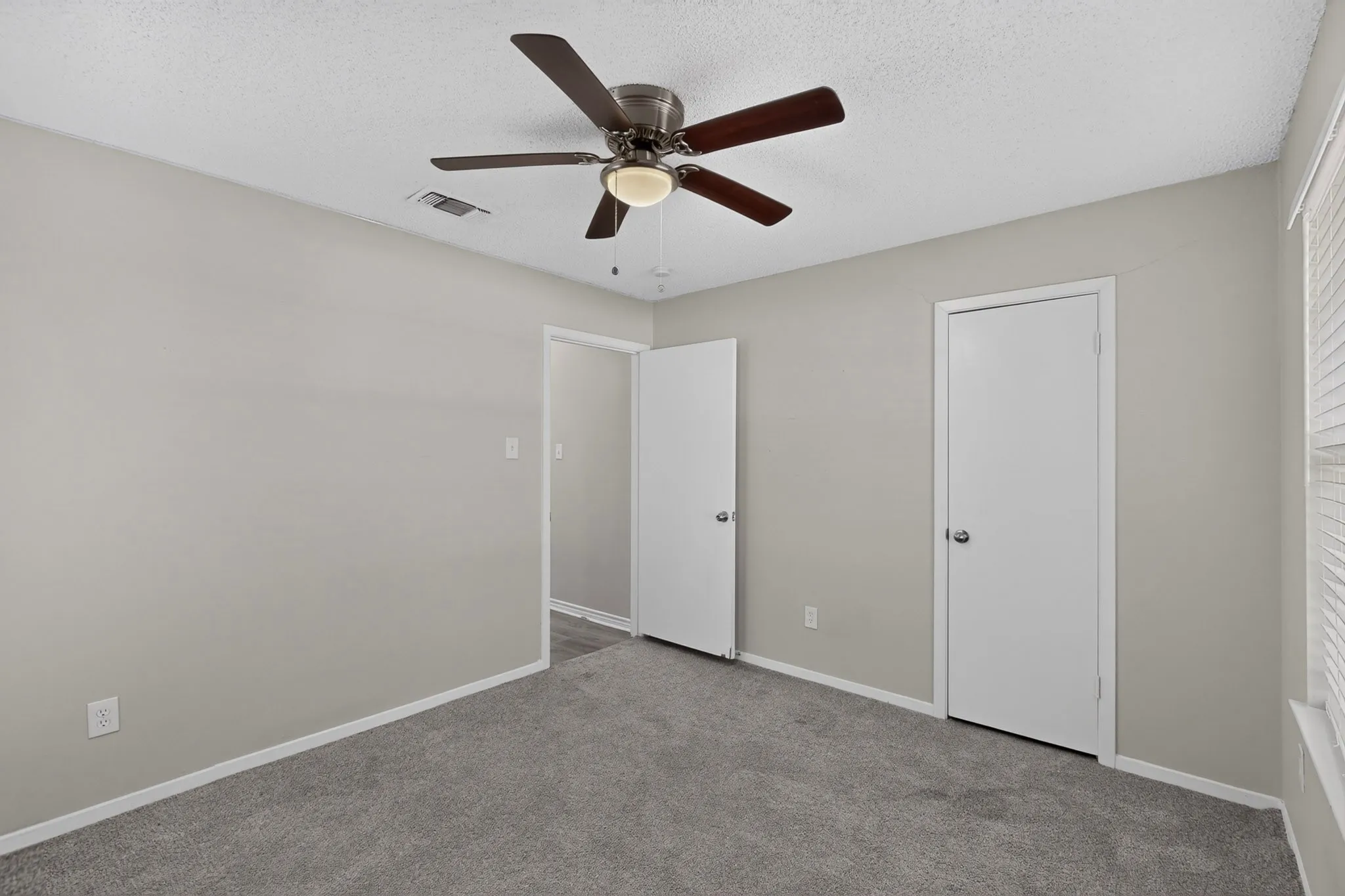 Plush grey carpeting, neutral wall paint, white trim, ceiling fan with light fixture, and white interior doors