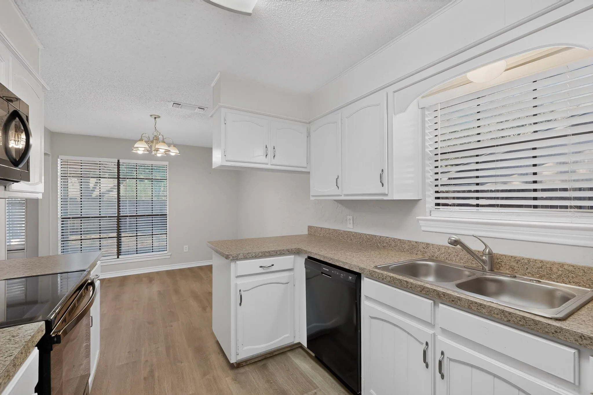 White cabinetry, wood-finish flooring, stainless steel double basin sink, and black dishwasher
