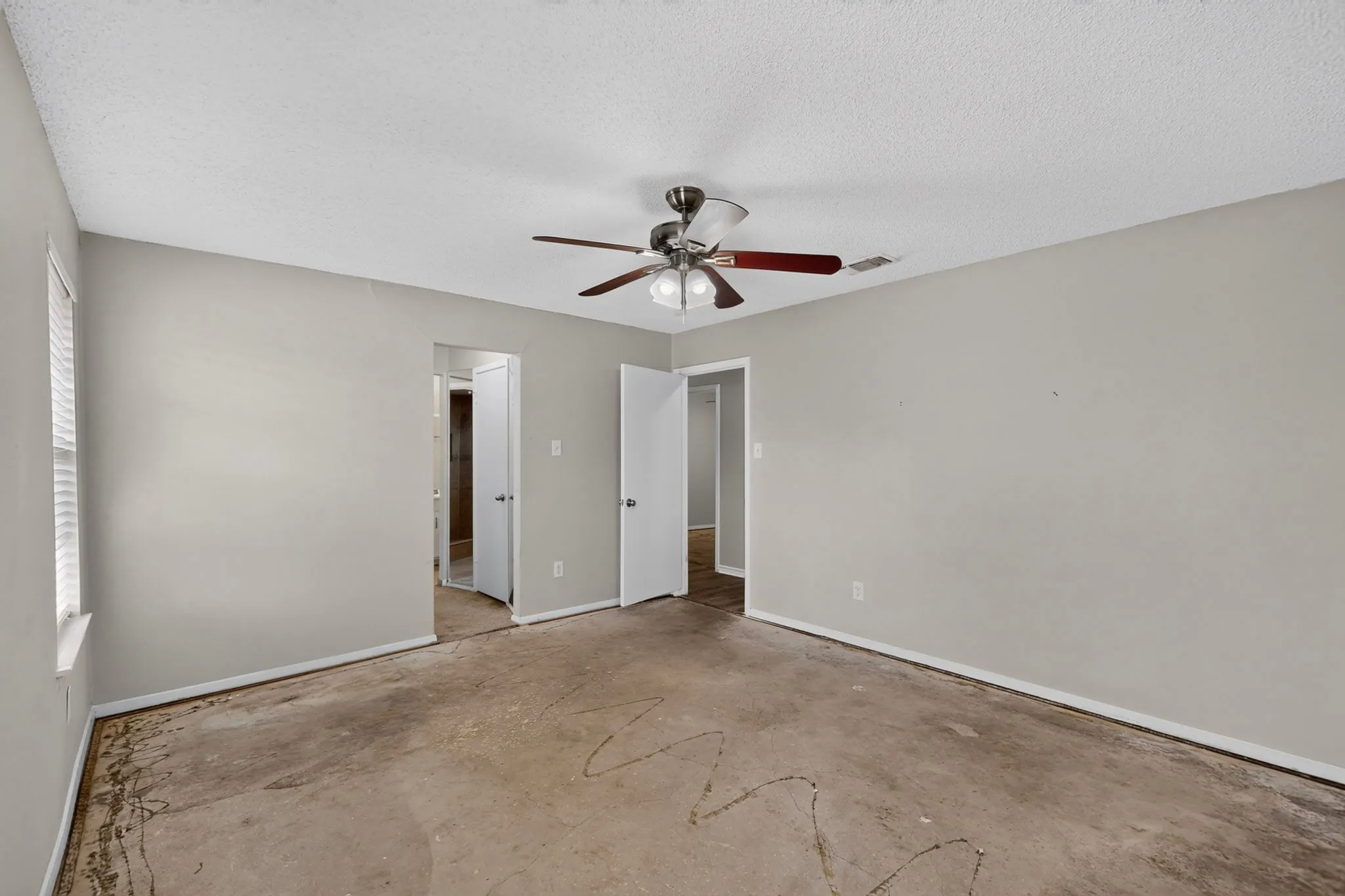 Spacious interior room with light gray walls, a textured ceiling, and a ceiling fan with light