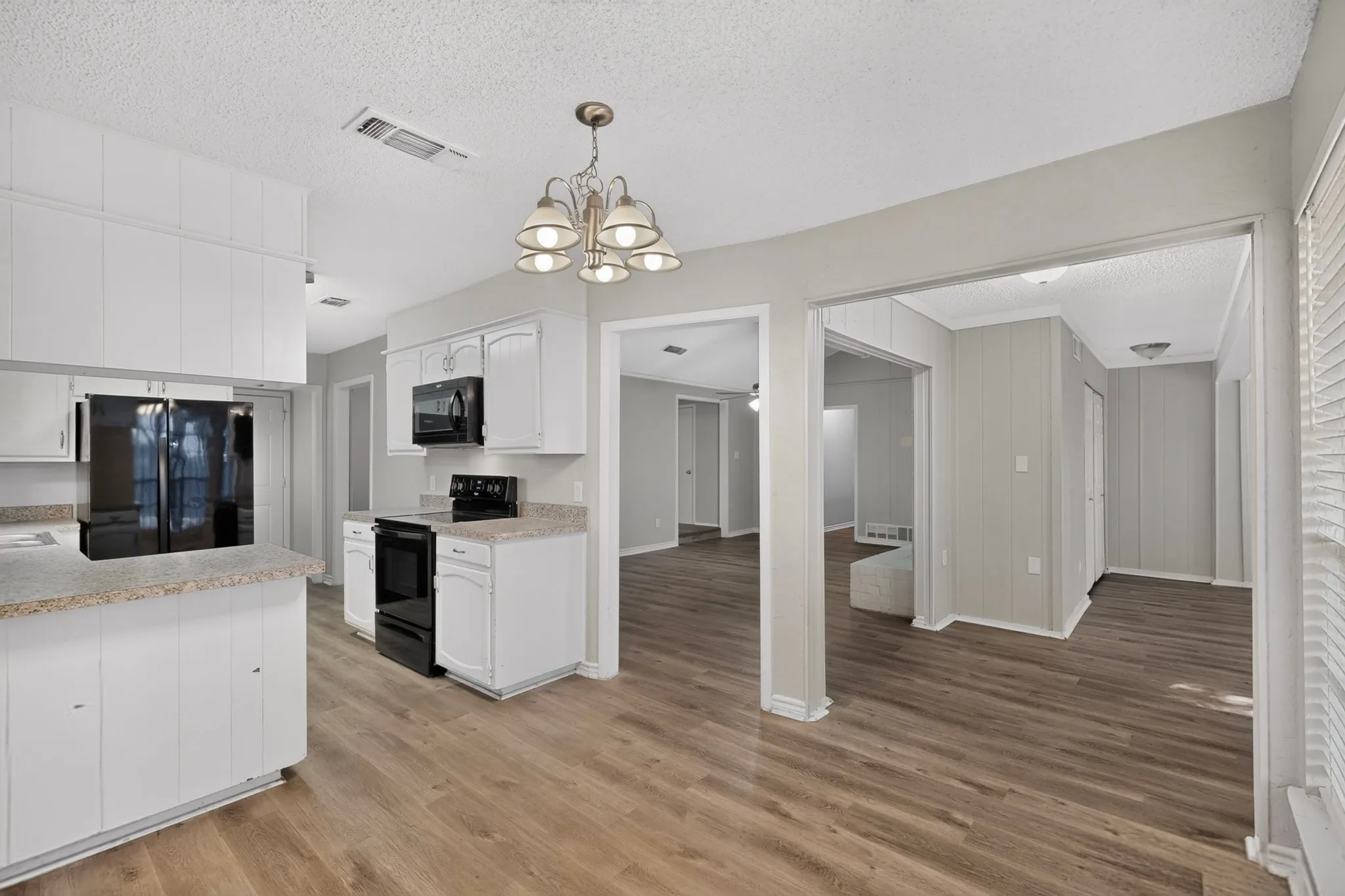 Kitchen featuring white cabinetry, black appliances, light-toned countertops, and wood-finish flooring