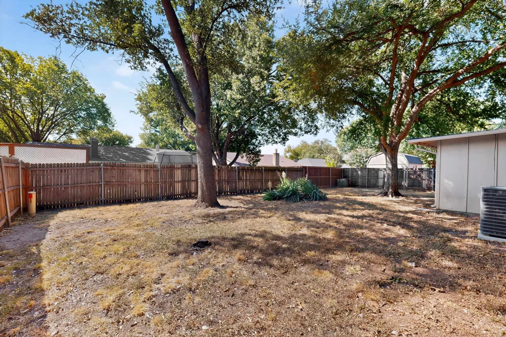 Spacious backyard retreat featuring mature shade trees, wooden perimeter fencing, and multiple outbuildings providing ample storage and utility space