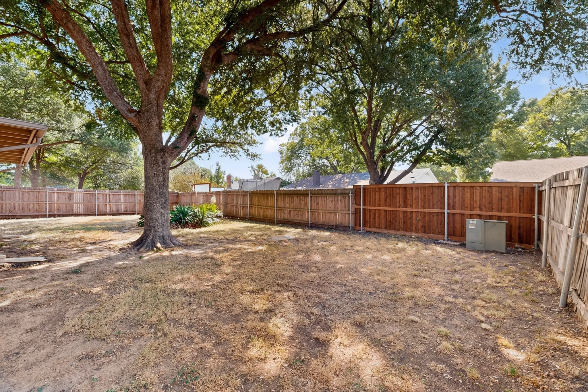 Spacious backyard featuring mature trees, surrounding wood fencing, and an outdoor utility unit