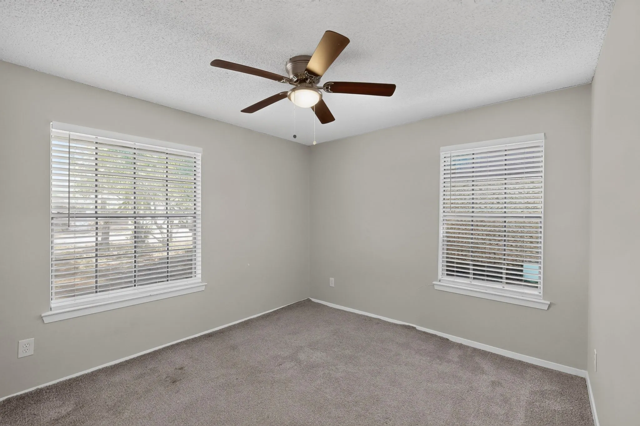 Light gray walls, textured ceiling, two windows with white blinds, and a ceiling fan with integrated lighting
