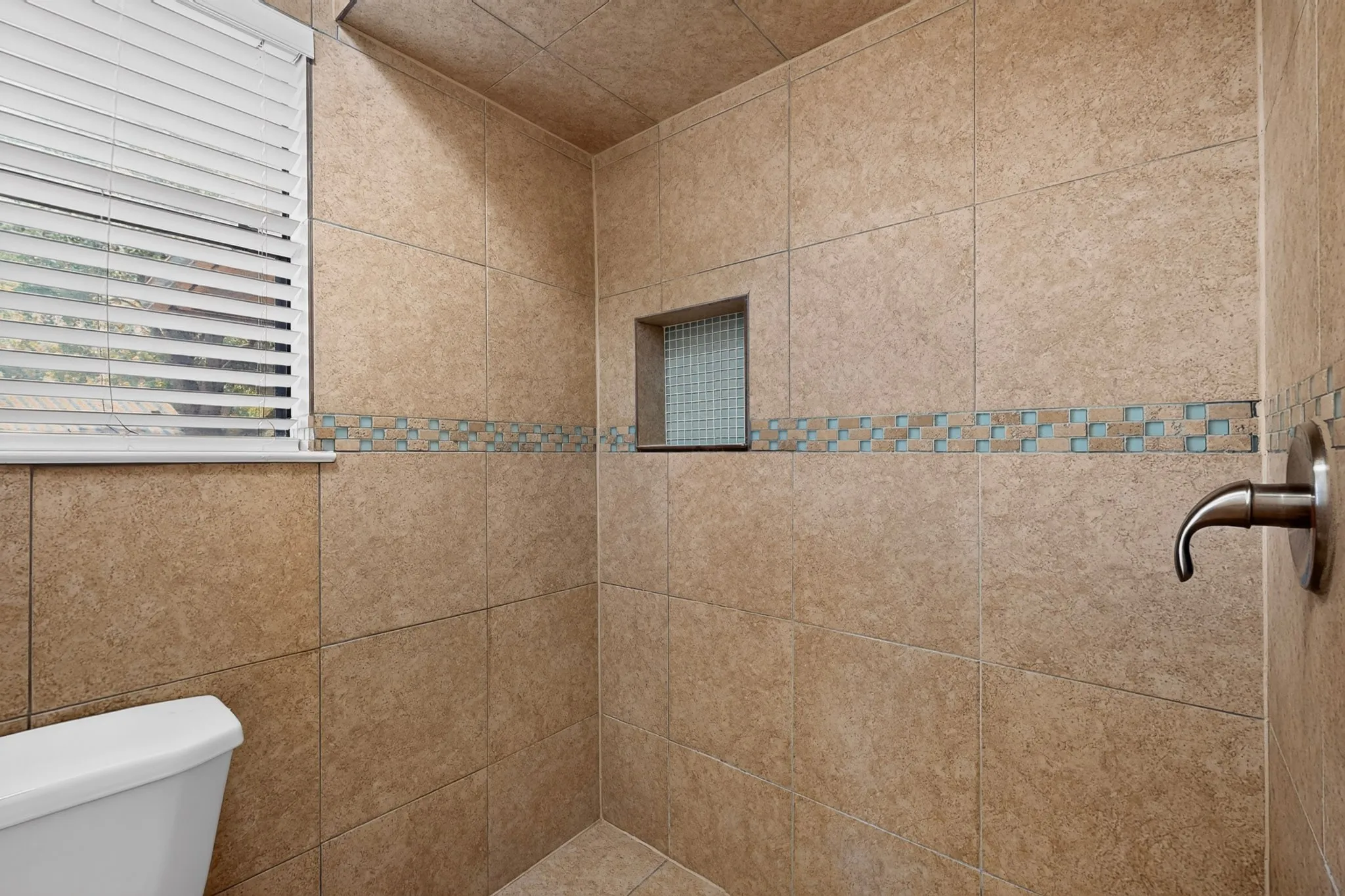 Tiled shower with an integrated niche, decorative mosaic tile band, and a brushed metal shower fixture