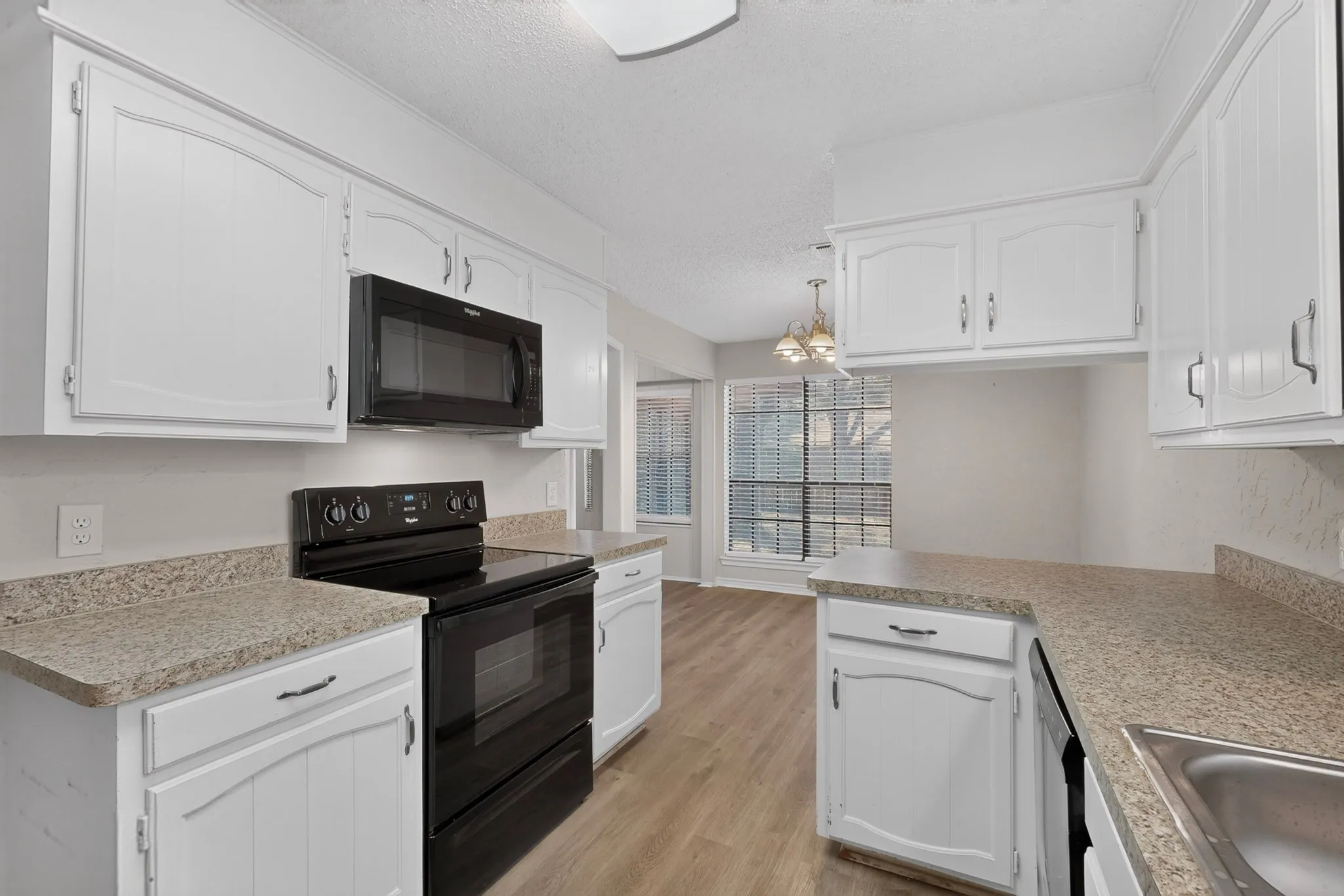 Kitchen featuring white cabinetry, light-toned countertops, black appliances, a stainless steel sink, and wood-finish flooring