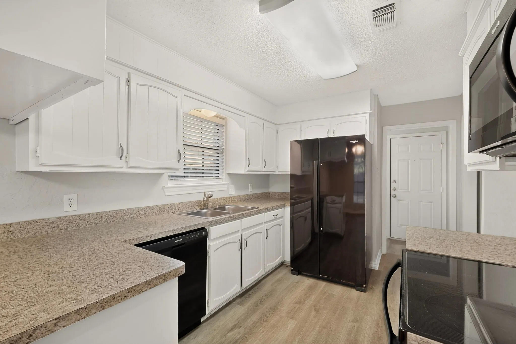 White cabinetry, wood-finish flooring, dark stone-finish countertops, and black appliances