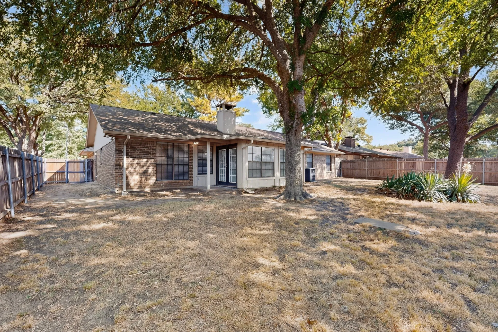 Expansive backyard featuring mature trees, a brick exterior, a covered patio, and a privacy fence