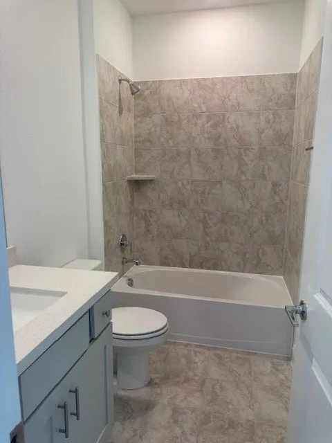 Bathroom featuring a built-in bathtub with shower, tiled surround, toilet, and vanity with an integrated sink and chrome hardware