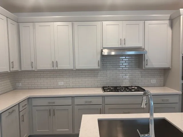 Shaker-style cabinetry, subway tile backsplash, stainless steel range hood, built-in gas cooktop, and undermount sink with a pull-down faucet