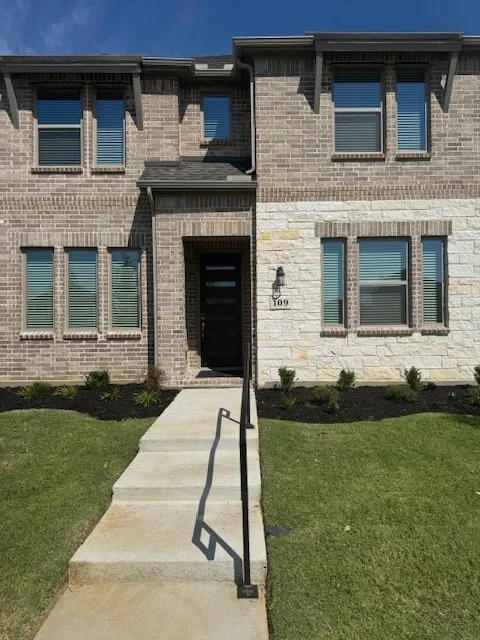 Two-story facade with mixed brick and stone cladding, multiple windows with blinds, front entry door, and a concrete walkway with a handrail