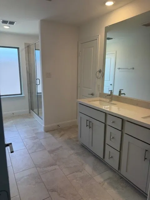 Dual sink vanity with light-toned countertop, glass-enclosed shower, light-toned tile flooring, and recessed lighting