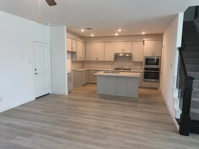 Open-concept layout featuring light wood-finish flooring, a contemporary kitchen island with seating, stainless steel appliances, a tiled backsplash, and recessed lighting