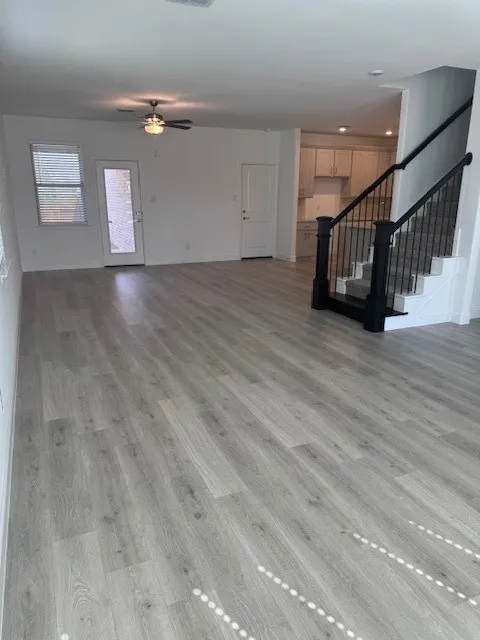 Open-concept living area featuring wood-finish flooring, a ceiling fan, and a glass-paneled exterior door with side window